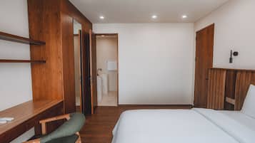 Habitación de hotel con un armario de madera, un escritorio con silla, una cama y un baño visible a través de una puerta abierta.