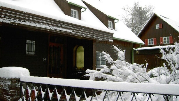 Een houten huis met een sneeuwbedekte kap en het nummer '19' op de zijkant.