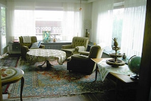 A room with a large window, a round table, two armchairs, a small table with a globe, and a patterned rug.