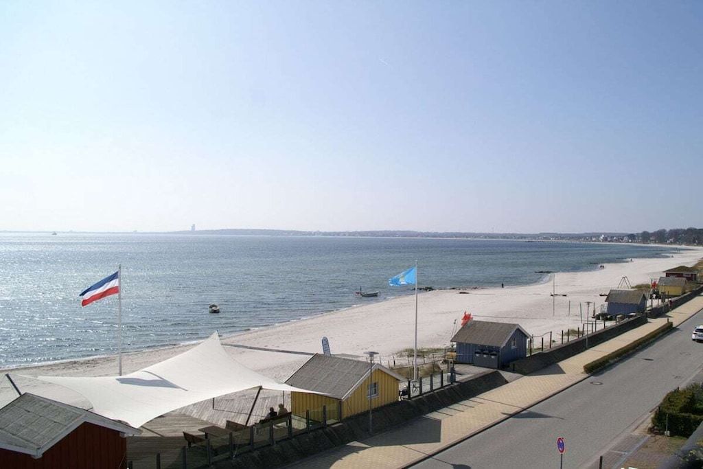 Una carretera costanera amb edificis a la vora de la platja, una bandera i una vista despejada del mar.