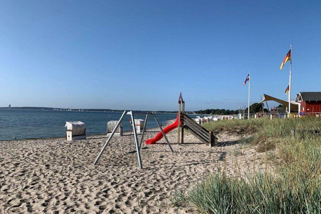 Une plage avec un toboggan rouge, une structure en bois et des drapeaux.