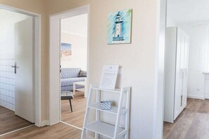 A room with a white door, a white shelf with a small item, and a painting of a lighthouse. - House Bärbel Apartment No. 5 (Cuxhaven)