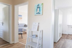 A modern interior with a white door, a small white shelf with a sign, and a painting of a lighthouse on the wall. - House Bärbel Apartment No. 6 (Cuxhaven)