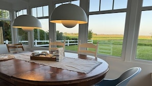 A round dining table with chairs, two pendant lights, and a view of a grassy field through large windows. - Holiday home in Langeoog with swimming pool (Langeoog)