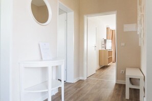 A hallway with a white console table, a mirror, and a door leading to a room with a wooden floor and a bed. - House Bärbel Apartment No. 4 (Cuxhaven)