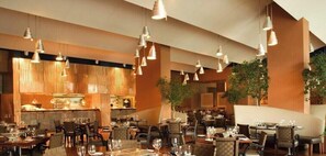 Ein Restaurant mit mehreren Tischen und Stühlen, hängenden Pendelleuchten und einer Bar.