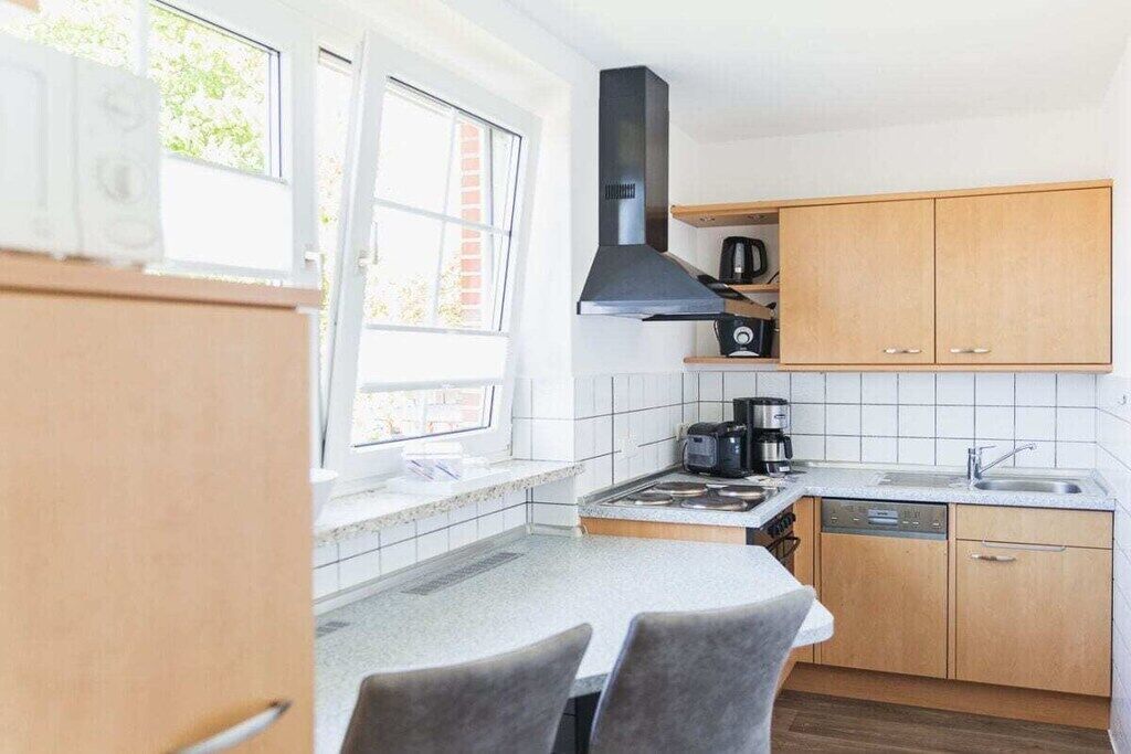 A compact kitchen with a window, a stove, a sink, and wooden cabinets.