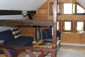 Ein Zimmer mit einem Etagenbett, einer Schlafcouch und einem Tisch mit einem Buch. Es gibt Fenster und eine Holzwand.