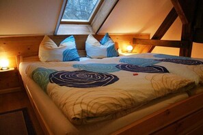 Ein gemütliches Schlafzimmer mit geneigter Decke, einem Bett mit gemustertem Duvet und zwei Nachttischlampen.