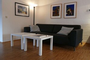 Ein Wohnzimmer mit einer schwarzen Couch, zwei weißen Tischen und drei gerahmten Kunstwerken an der Wand.