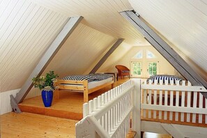 A loft bedroom with a sloped ceiling, two beds, a wooden floor, a white railing, and a potted plant. - Holiday home with 3 bedrooms (Reichshof-Heischeid)