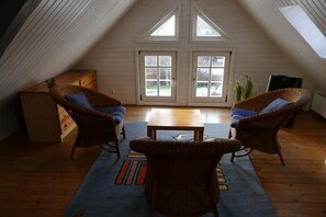 An attic room with two wicker chairs, a wooden table, and a large window. - Holiday home with 3 bedrooms (Reichshof-Heischeid)
