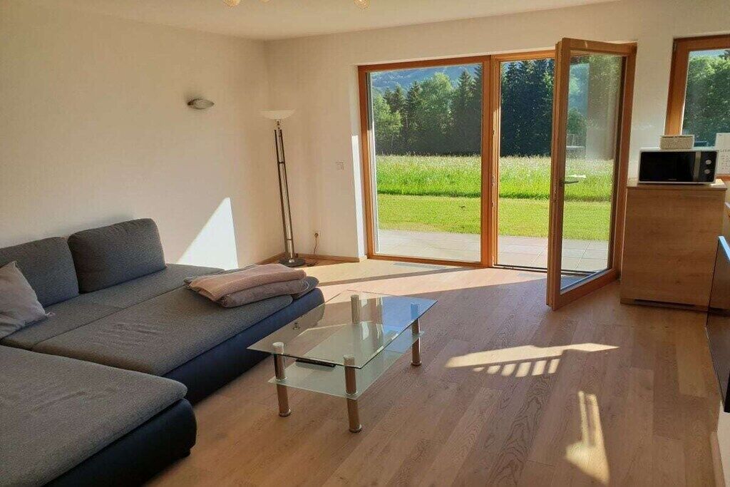 Ein modernes Wohnzimmer mit einer Couch, einem Glastisch und einer Glasschiebetür, die zu einem Garten führt.