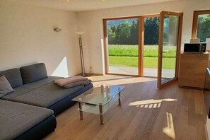 A modern living room with a sofa, a glass coffee table, and a sliding glass door leading to a garden. - Holiday apartment with 2 bedrooms (Aurach bei Kitzbühel)