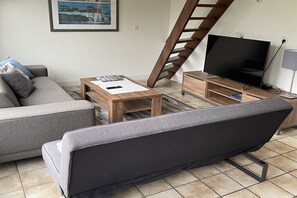 Un salon comprenant un canapé, une table basse, un meuble pour la télévision et un escalier.