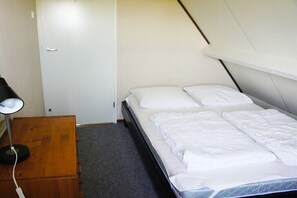 A small, single-bed room with a wooden dresser, a desk with a lamp, and a white door. - Holiday home with 3 bedrooms (Sint Maartensvlotbrug)