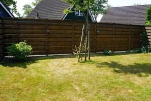 A wooden fence, a grassy yard, and a house with a tiled roof. - Holiday home with 3 bedrooms (Sint Maartensvlotbrug)