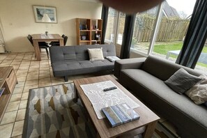 A living room with a sofa, a coffee table, a dining table, and a bookshelf. - Holiday home with 3 bedrooms (Sint Maartensvlotbrug)