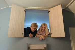 Une pièce dans laquelle la porte d’un meuble en bois est ouverte, révélant deux personnes penchées à l’intérieur.