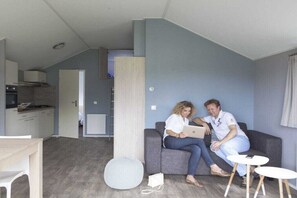 Ein modernes Wohnzimmer mit einem grauen Sofa, einem kleinen runden Tisch und einer Küchenzeile im Hintergrund.