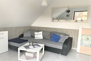 A modern living room with a sofa, a coffee table, and a small white cabinet. - Holiday apartment with 1 bedroom (Wangerland)