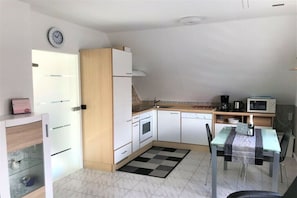 A compact kitchen with white cabinets, a microwave, a coffee maker, and a small dining table with chairs. - Holiday apartment with 1 bedroom (Wangerland)