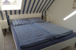 Une chambre à coucher avec un lit, des tables de chevet, une fenêtre et un plafond en pente.