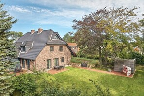 A two-story stone house with a sloped roof, a patio with outdoor furniture, and a small wooden structure. - Holiday home in St. Peter-Ording with sauna (St.Peter-Ording)