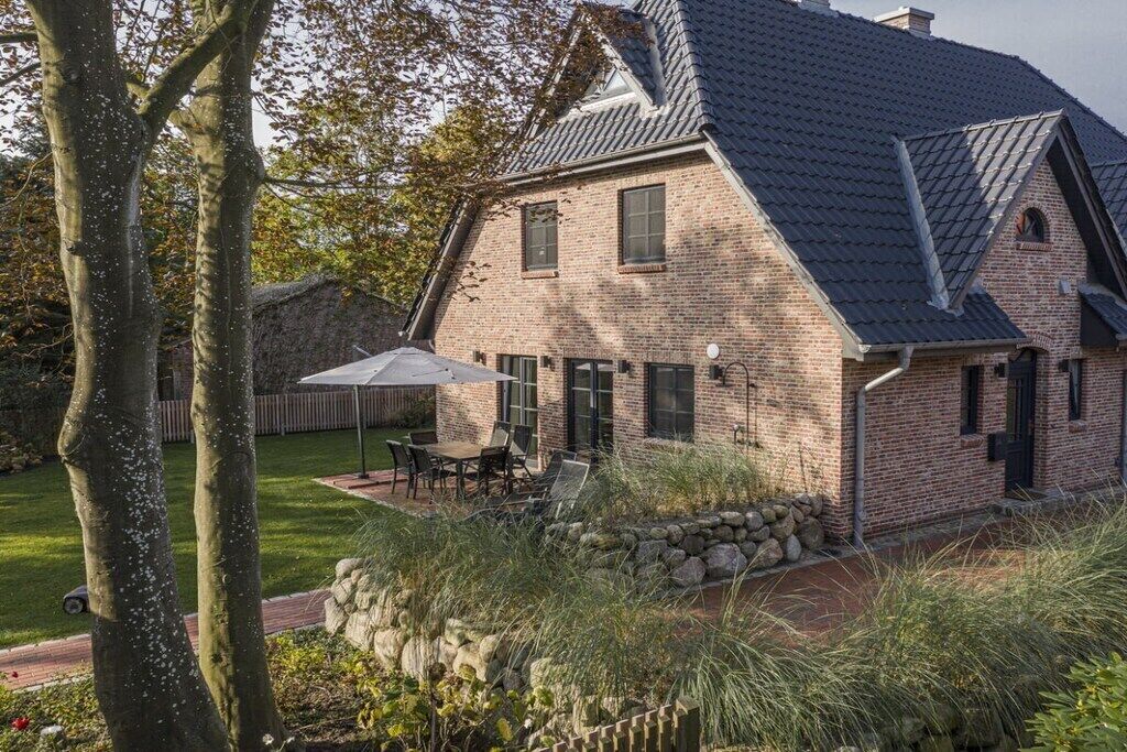 A brick house with a sloped roof, a patio with outdoor furniture, and a stone wall.