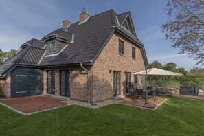 A two-story brick house with a dark roof, a garage, and a patio with outdoor furniture. - Holiday home in St. Peter-Ording with sauna (St.Peter-Ording)