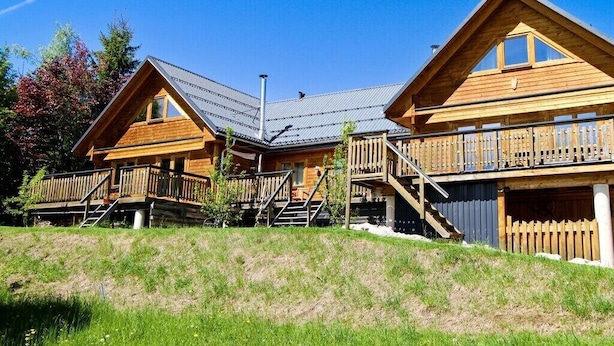 En træhytte med skråt tag, en balkon og en trappe, der fører op til øverste etage.