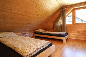 A room with two wooden beds, a window with a curtain, and a wooden ceiling.