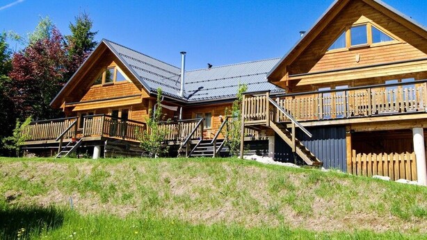 A wooden cabin with a sloped roof, a balcony, and a staircase leading to the upper level.