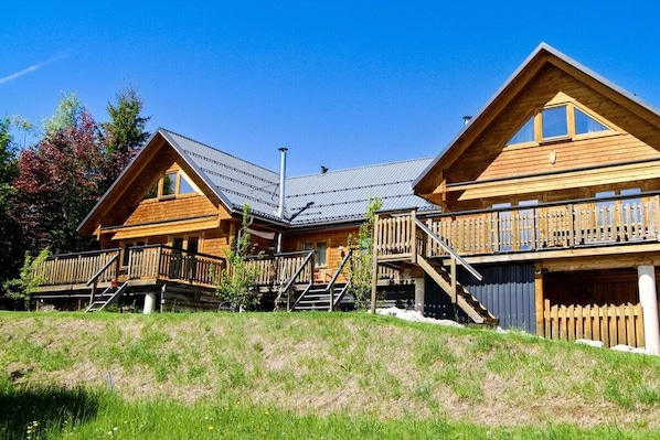 A wooden cabin with a sloped roof, a balcony, and a staircase leading to the upper level.