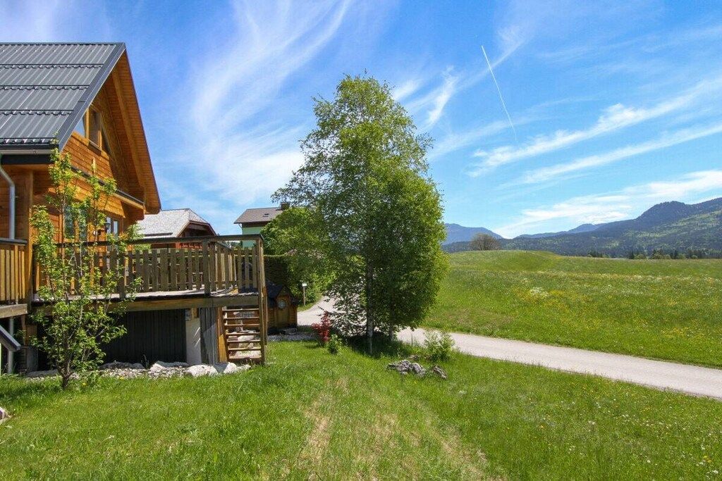 Eine Holzhütte mit einer Veranda, umgeben von einer Wiese und Bergen im Hintergrund.