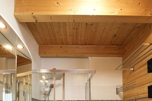 A modern bathroom with wooden ceiling beams, a glass shower enclosure, and a white tiled wall.