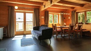 A wooden cabin interior with a sofa, dining table, chairs, and a fireplace.