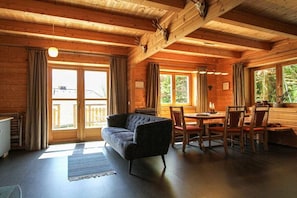 A wooden cabin interior with a sofa, dining table, chairs, and a fireplace.