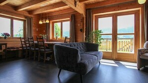 A wooden cabin interior with a dining area, a sofa, and large windows offering a view of the outdoors.