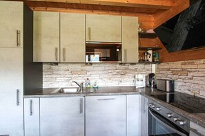 A modern kitchen with stainless steel appliances, a stone backsplash, and wooden beams. - Cabin with 3 bedrooms (Bad Mitterndorf)