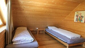 A small, single-room cabin with two beds, a wooden ceiling, and a window with curtains.