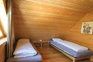 A small, single-room cabin with two beds, a wooden ceiling, and a window with curtains.