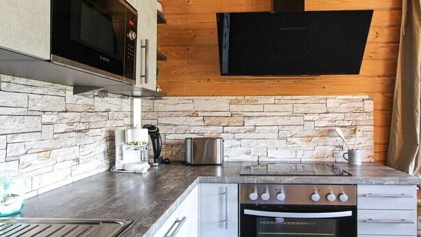 A kitchen with a stone backsplash, a microwave, a toaster, a coffee maker, and a stove.