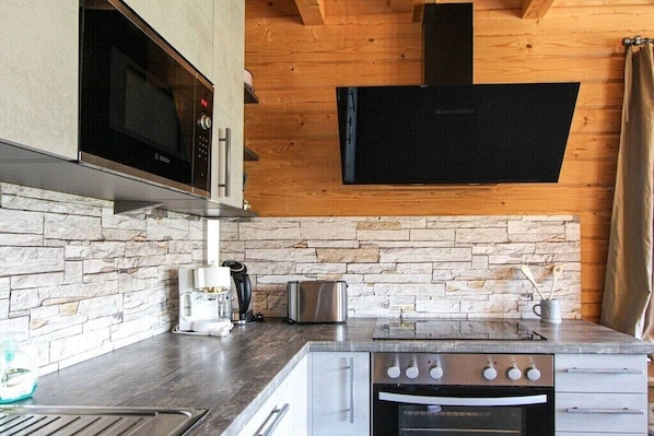 A kitchen with a stone backsplash, a microwave, a toaster, a coffee maker, and a stove.