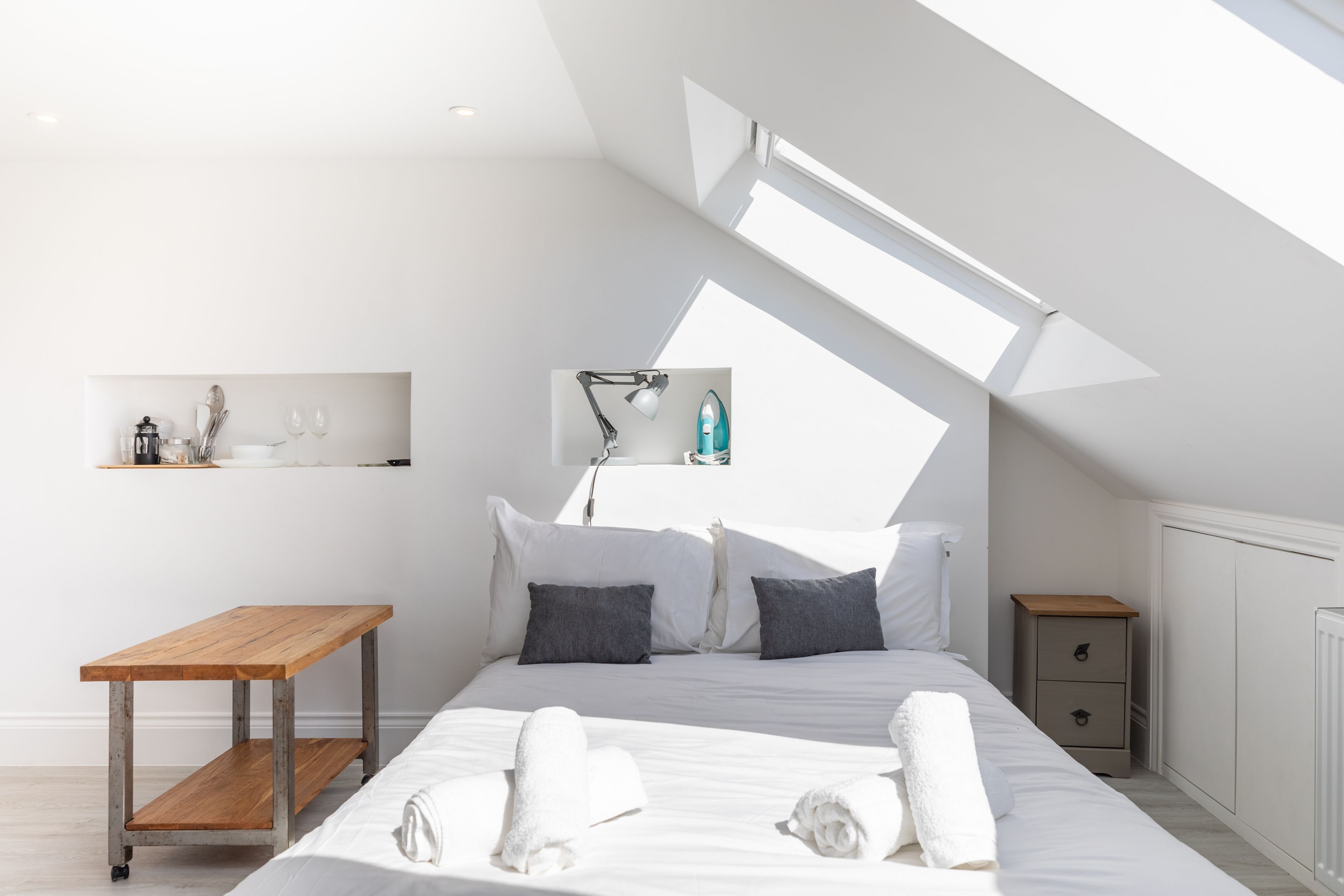 A modern bedroom with a skylight, a wooden table, a bedside drawer, and neatly folded towels.