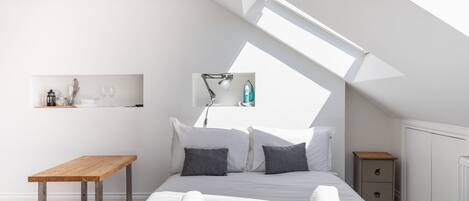 A modern bedroom with a skylight, a wooden table, a bedside drawer, and neatly folded towels.