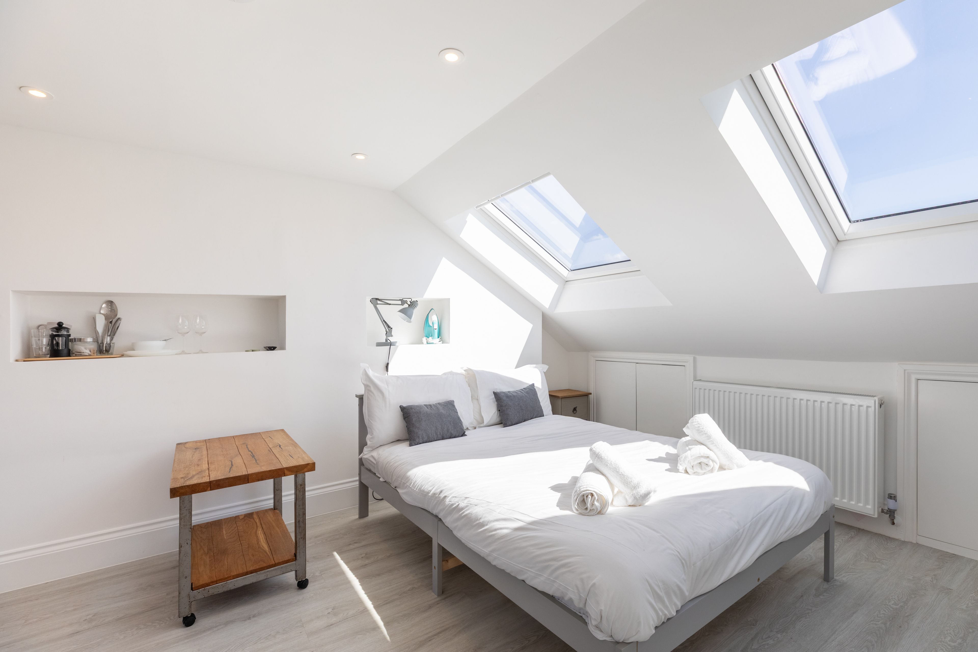 Ein modernes Schlafzimmer mit Oberlichter, einem Bett mit weißen Leinen, einem kleinen Holztisch und einer Heizung.