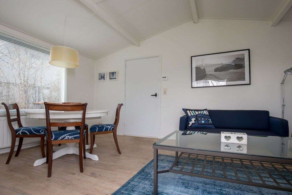Ein Zimmer mit Esstisch, zwei Stühlen, einer Couch, einem Glastisch, einem blauen Teppich und einem gerahmten Bild an der Wand.