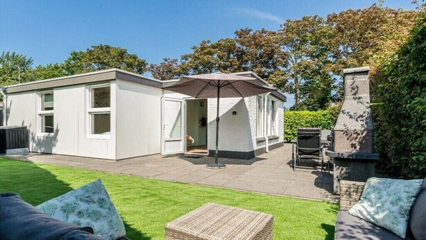 Eine moderne Außenpatio mit einem weißen Gebäude, einem Korbsessel und einem grauen Sofa mit Kissen.