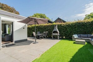A patio area with a barbecue grill, outdoor seating, and a white building. - Holiday home in Renesse with swimming pool (Renesse)